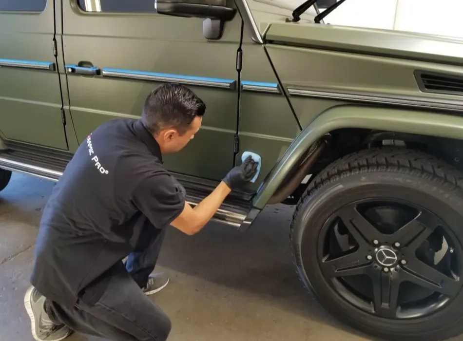 Person cleaning the fender of a green Mercedes-Benz SUV with a cloth in a garage.