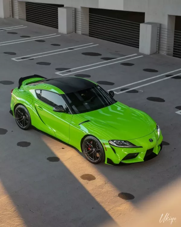 A bright green sports car parked in an empty parking lot with sunlight casting shadows.