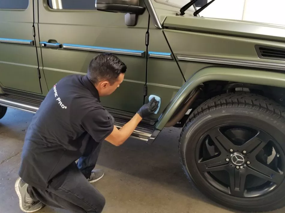Man cleaning the side of a green Mercedes-Benz SUV with a cloth inside a garage.