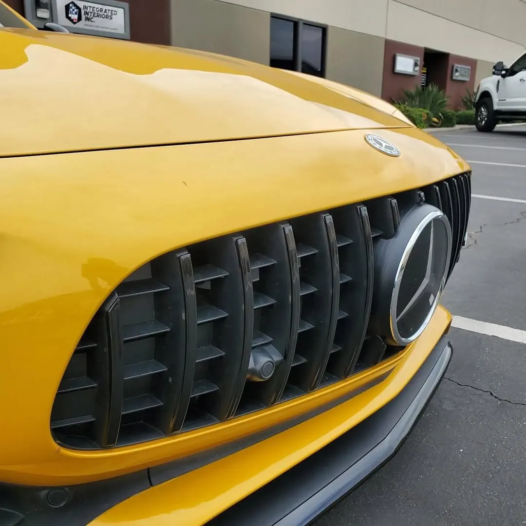 chrome-del-2 Close-up of a yellow Mercedes-Benz front grille and emblem in a parking lot.