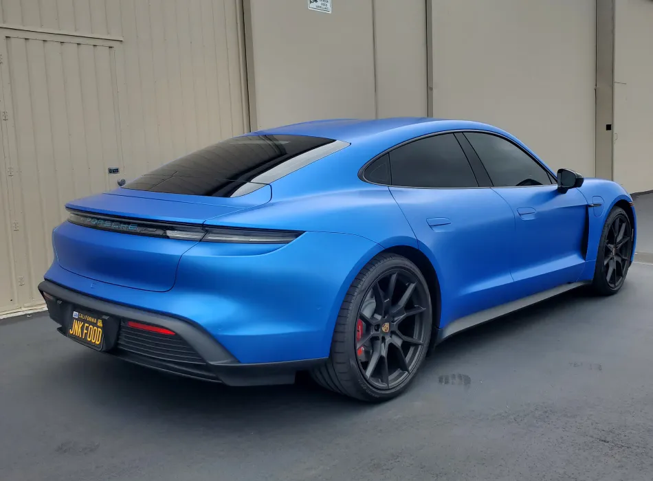 color-1 A matte blue electric sports car parked on a paved surface near beige industrial buildings.