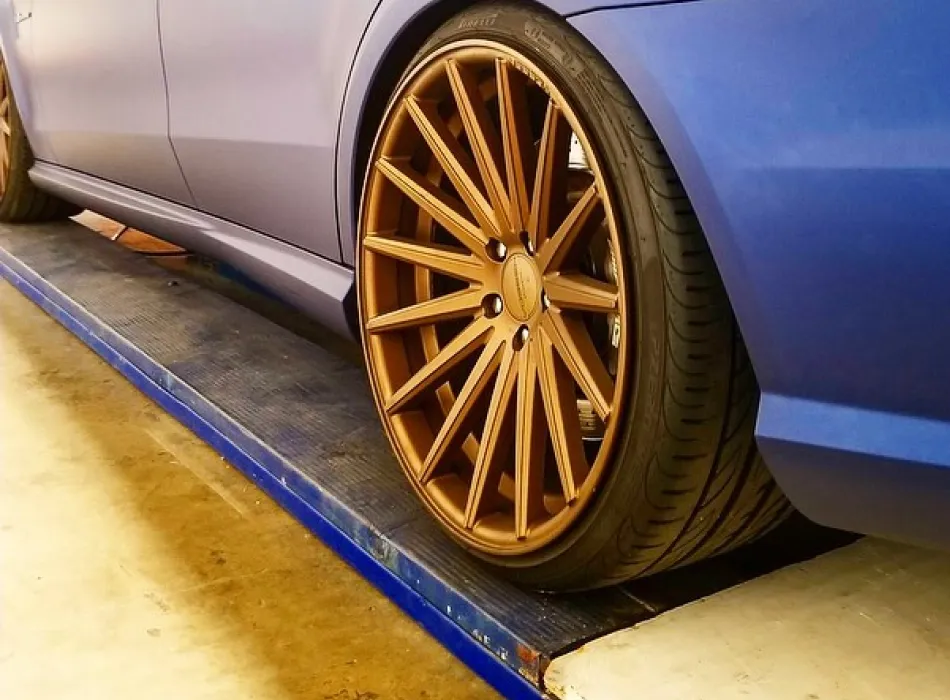 Close-up of a blue car with large bronze multi-spoke alloy wheels on a service ramp.
