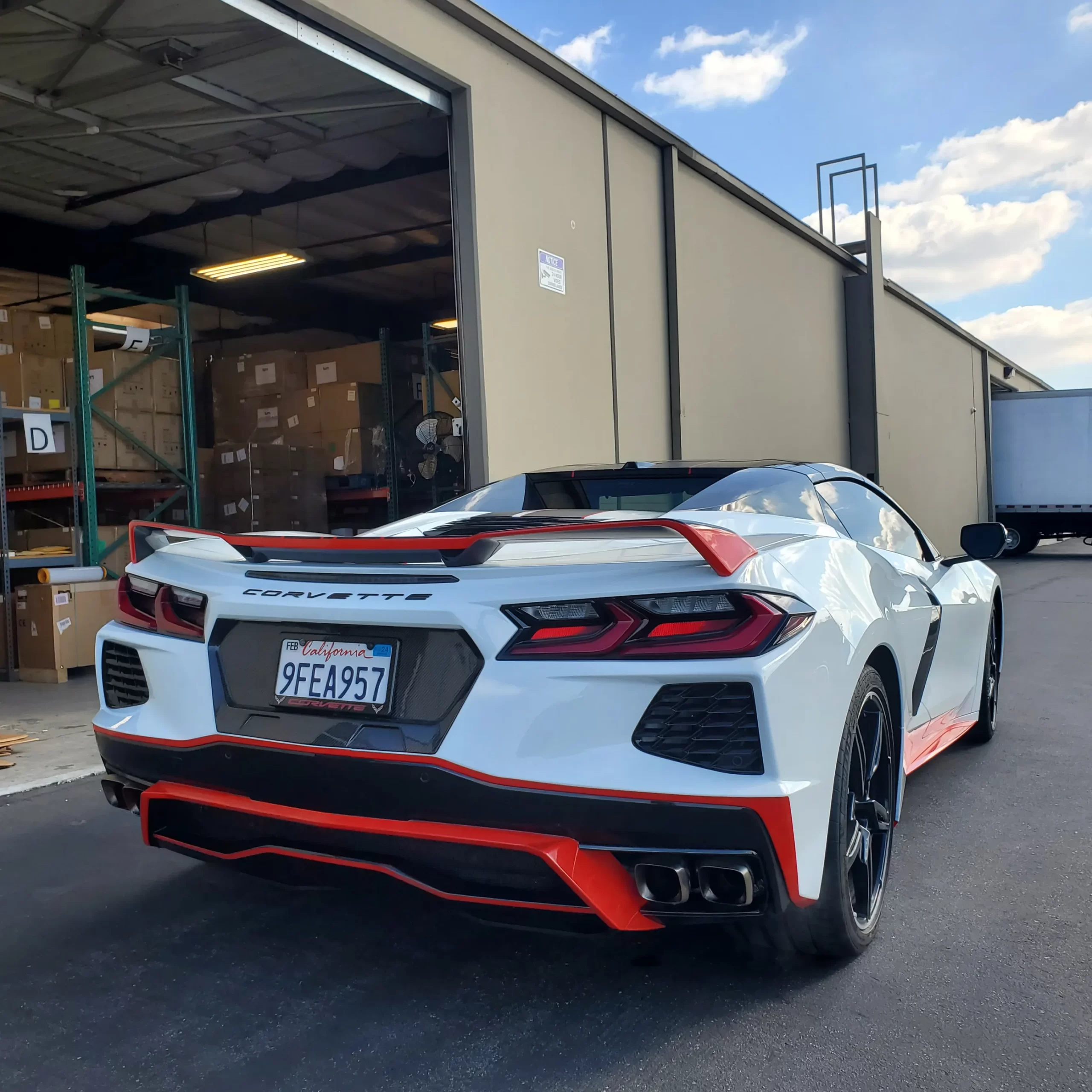 A white Chevrolet Corvette sports car with red accents parked outside a warehouse loading dock.