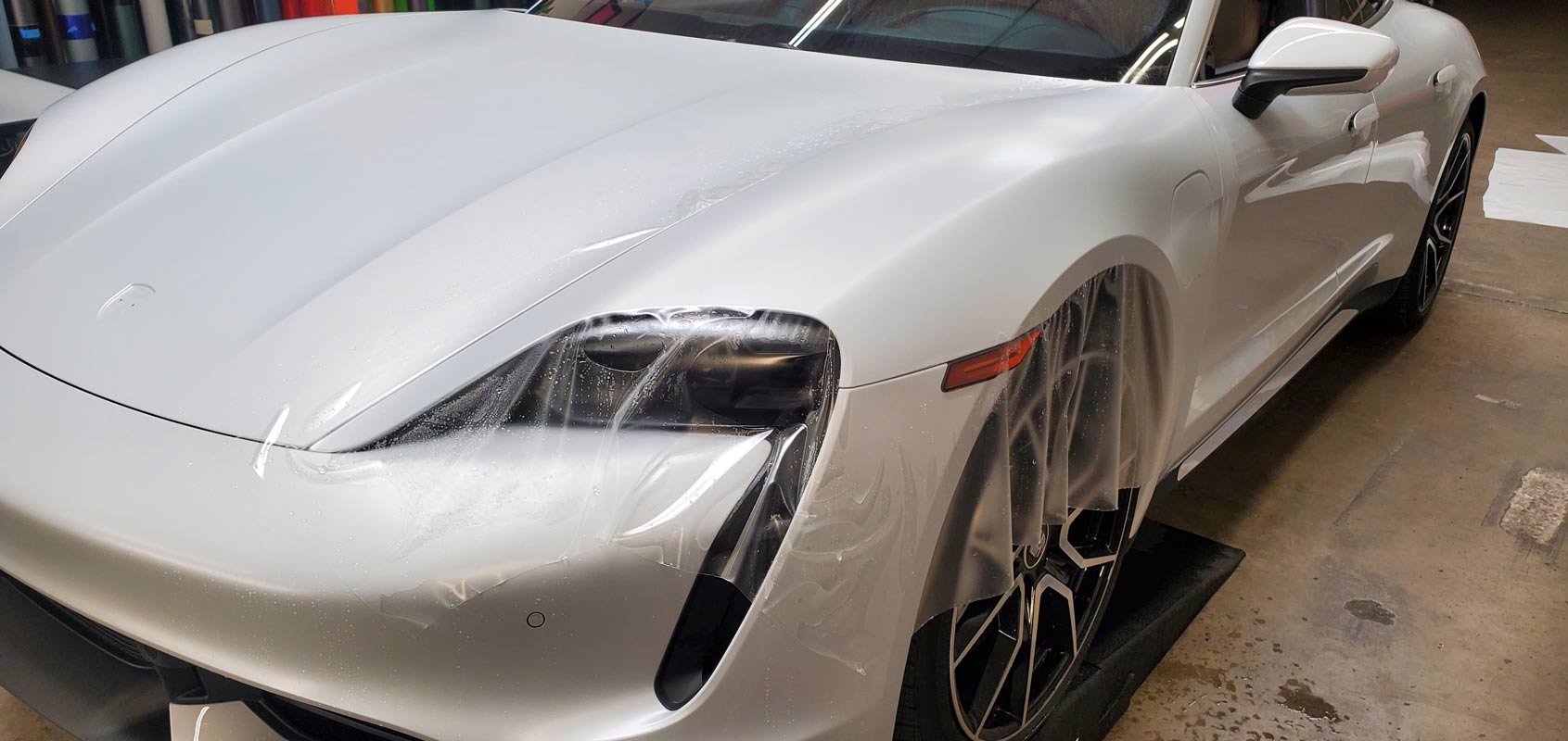 20240305_102804 A white sports car with a protective film being applied to the front hood and fender in a garage.